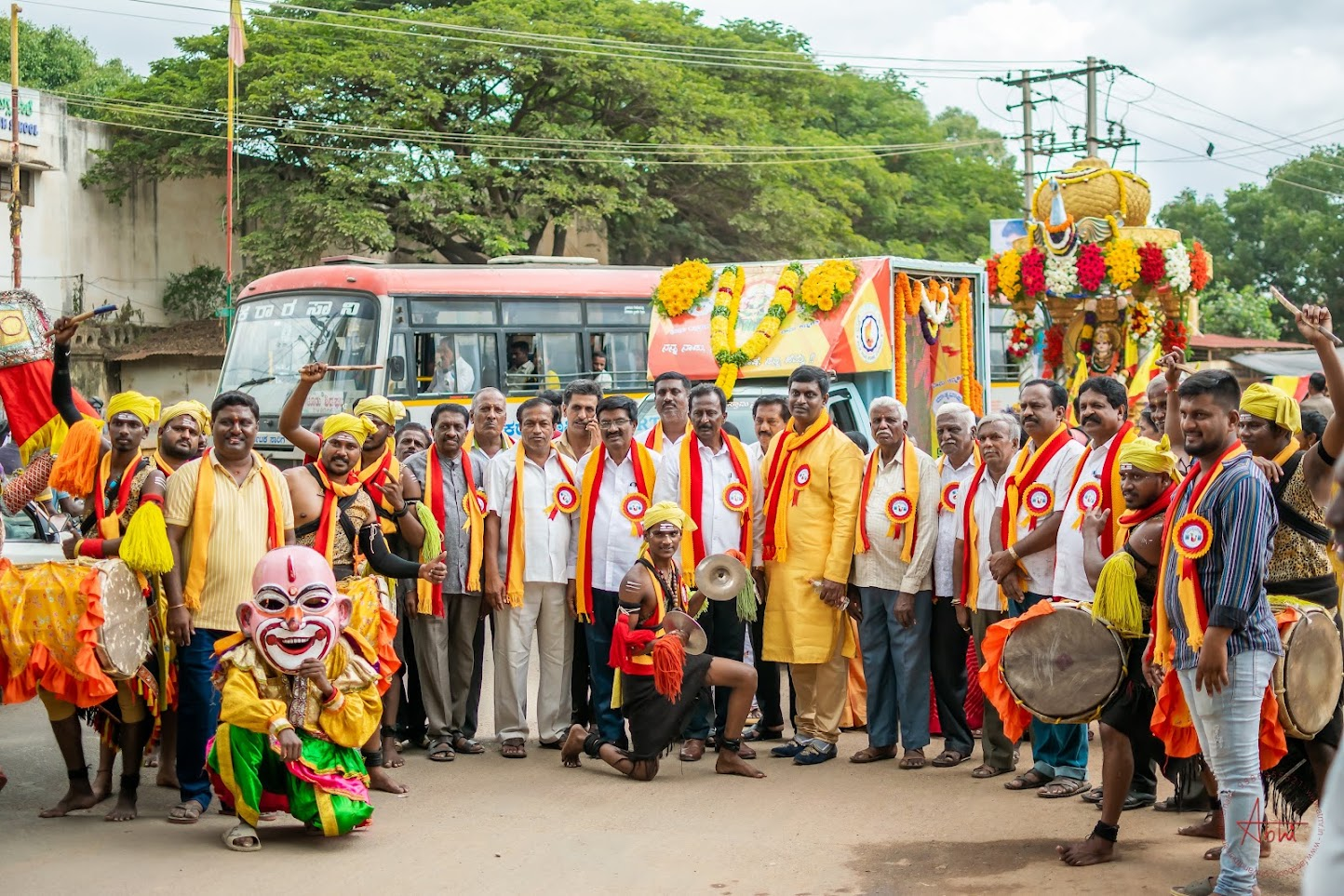 Community members in front of a decorated bus during the Rajyotsava procession, with drummers